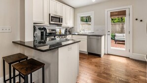 A modern kitchen with white cabinets, a central island, and a view to a patio. - Private Patio |German Village| Walk Everywhere (Columbus)