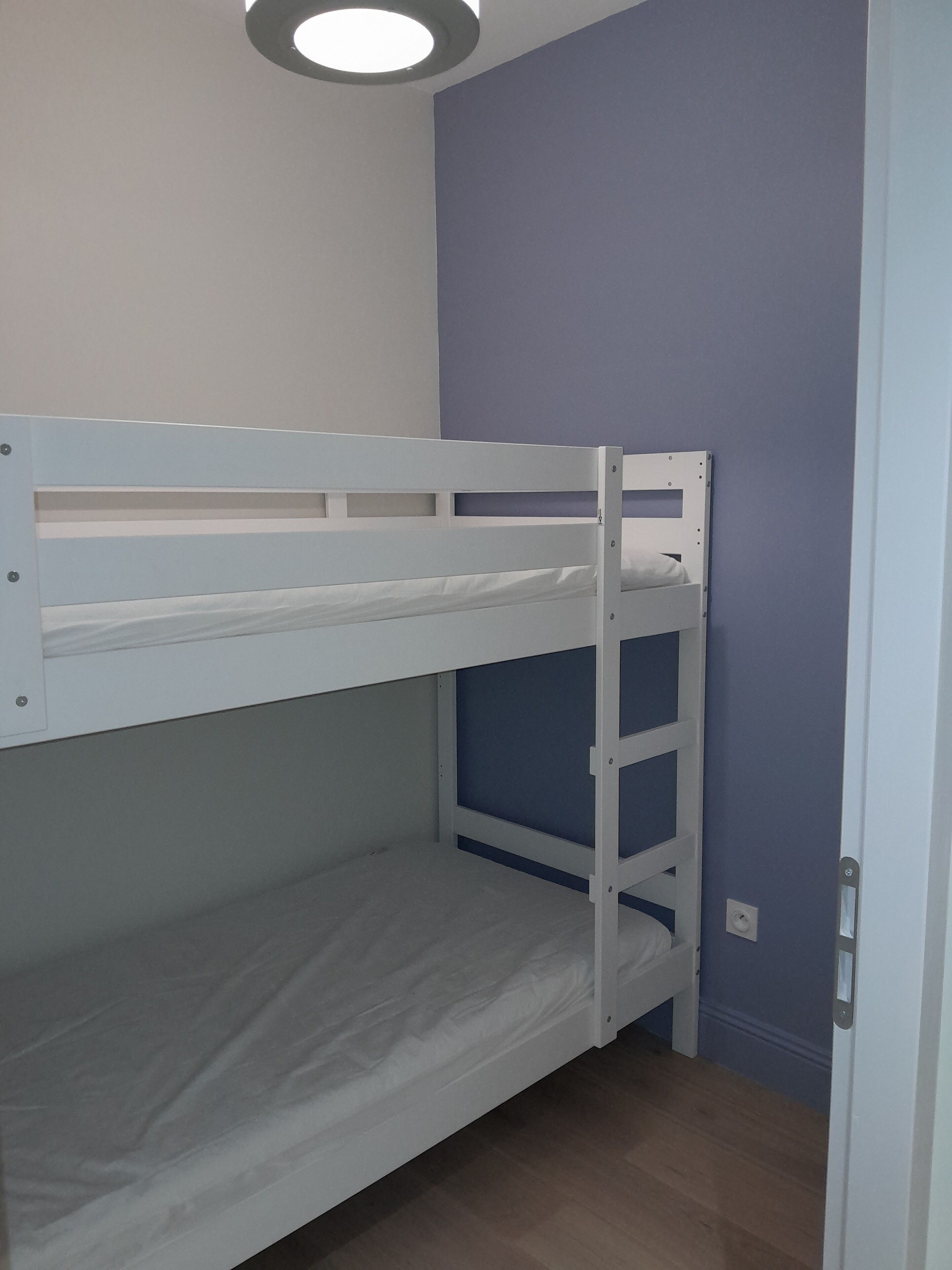 Una cama individual en un dormitorio con paredes azul claro y piso de madera.