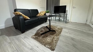 A modern living room with a black leather sofa, a glass coffee table, and a TV on a glass stand.