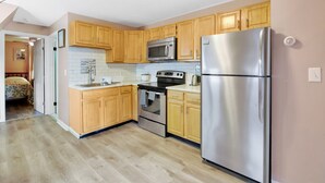 A compact kitchen with wooden cabinets, a stainless steel refrigerator, a microwave, and an oven.