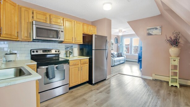 A modern kitchen with wooden cabinets, stainless steel appliances, and a view to the living area.