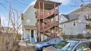 A two-story building with a wooden staircase and balcony, surrounded by other residential buildings.