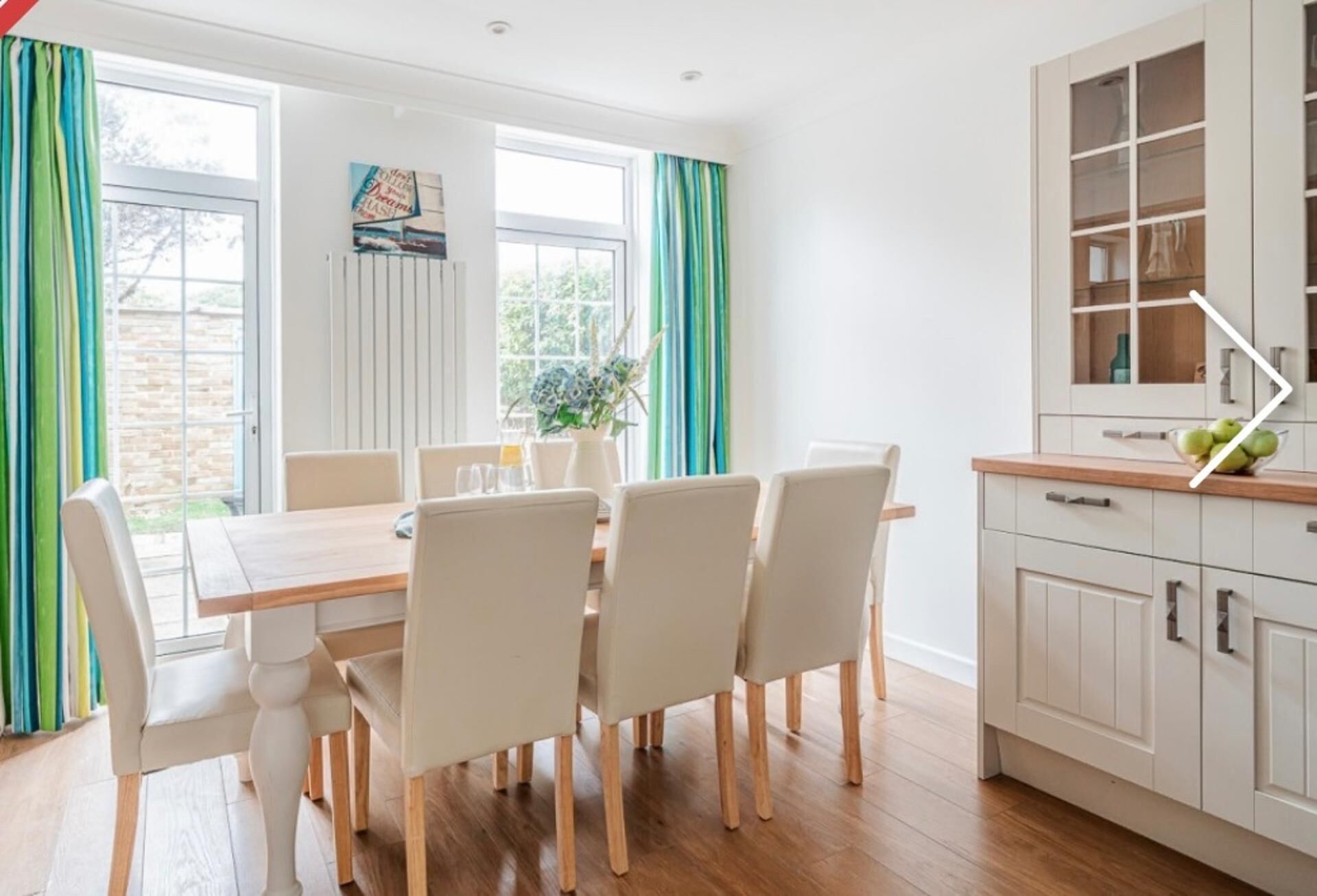 Een eethoek met een houten tafel en stoelen, een keuken met kastjes, en een raam met gordijnen.
