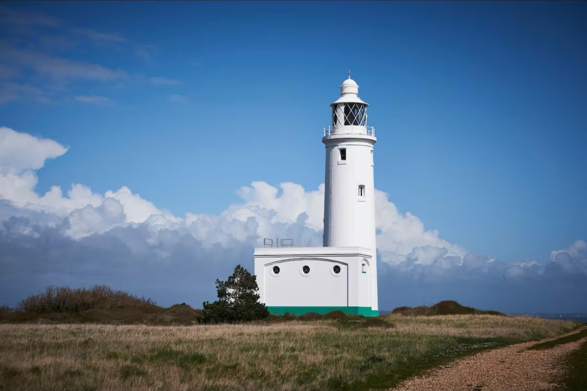 A white lighthouse with a green base, surrounded by a grassy field and a clear sky.