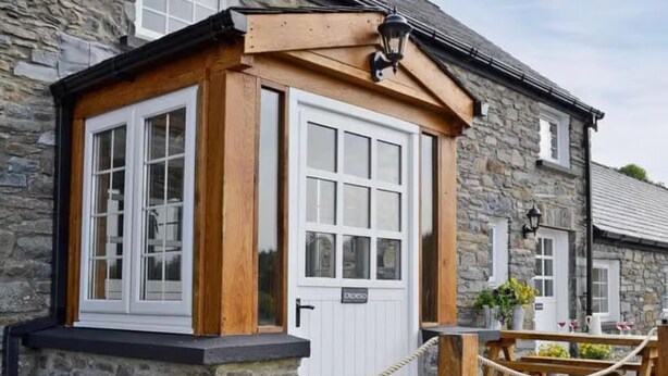 A stone building with a wooden door and windows, a rope barrier, and potted plants. - Golygfar Mynydd Retreat - Sleeps 6 (Tregaron)