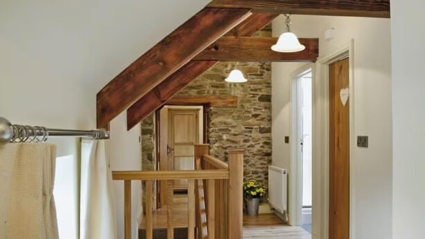 A wooden staircase with a stone wall background, a wooden railing, and a hanging light fixture. - Golygfar Mynydd Retreat - Sleeps 6 (Tregaron)