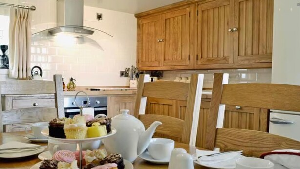 A dining area with a three-tiered dessert stand, a white teapot, and a wooden cabinet in the background. - Golygfar Mynydd Retreat - Sleeps 6 (Tregaron)