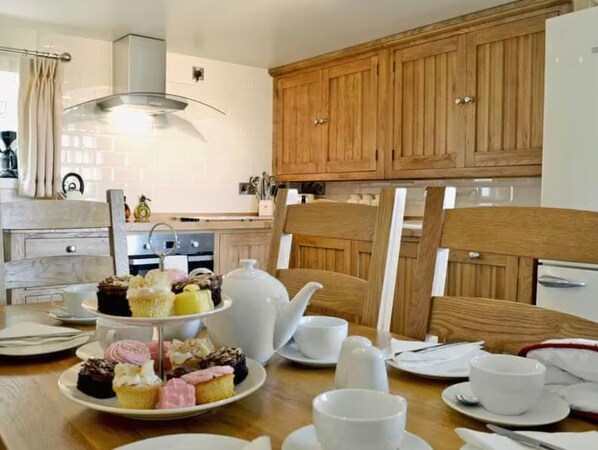 A dining area with a three-tiered dessert stand, a white teapot, and a wooden cabinet in the background. - Golygfar Mynydd Retreat - Sleeps 6 (Tregaron)