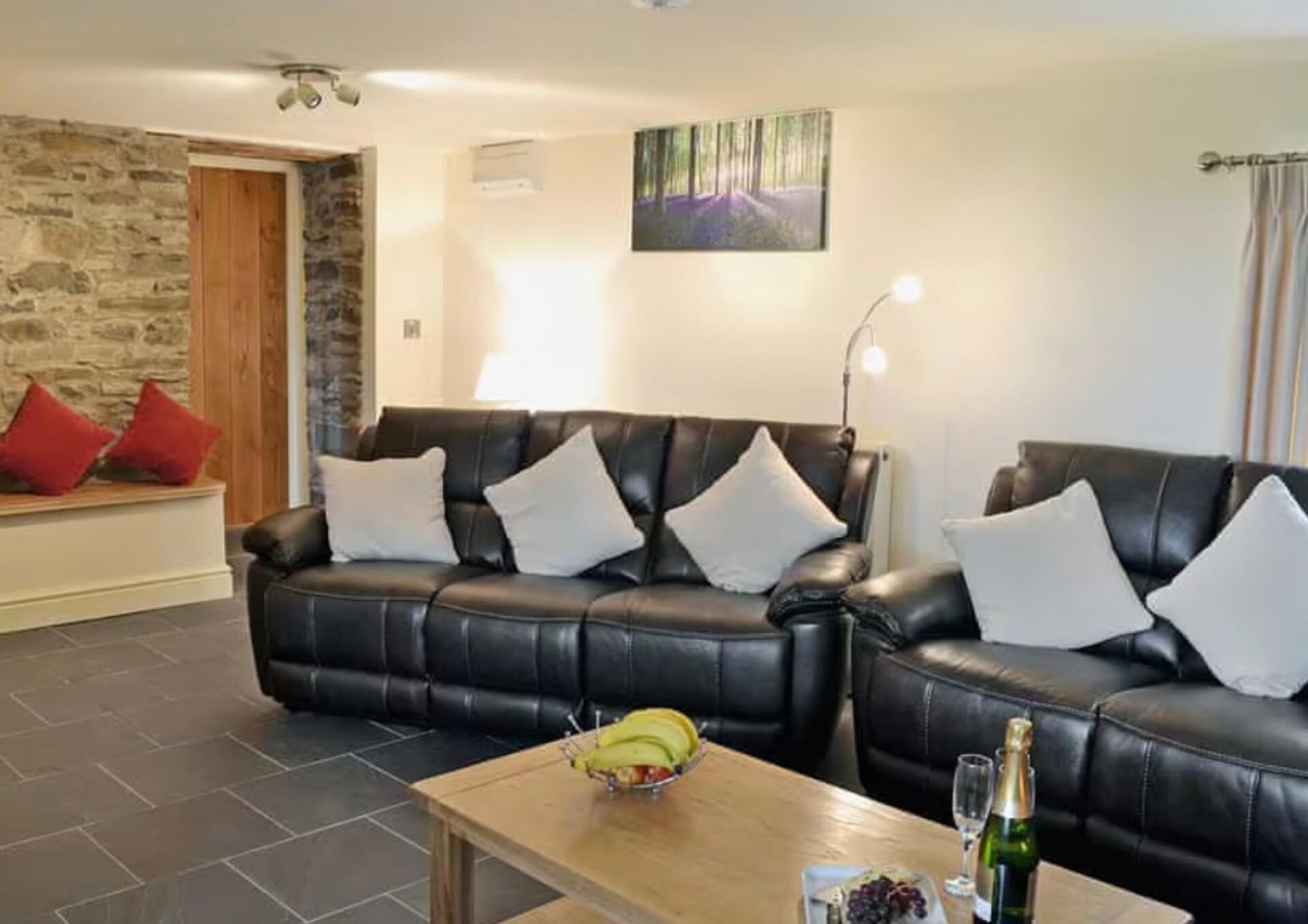 A living room with two black leather sofas, a wooden coffee table with fruits and a bottle, and a stone wall.