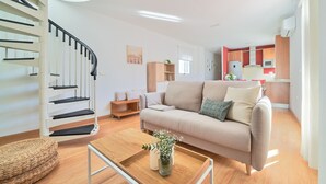 A modern living room with a staircase, a sofa, a coffee table, and a kitchen area in the background.