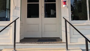 L’entrée d’un bâtiment, avec une enseigne indiquant « Musée de la coiffure » et un poteau rayé de rouge et de blanc.