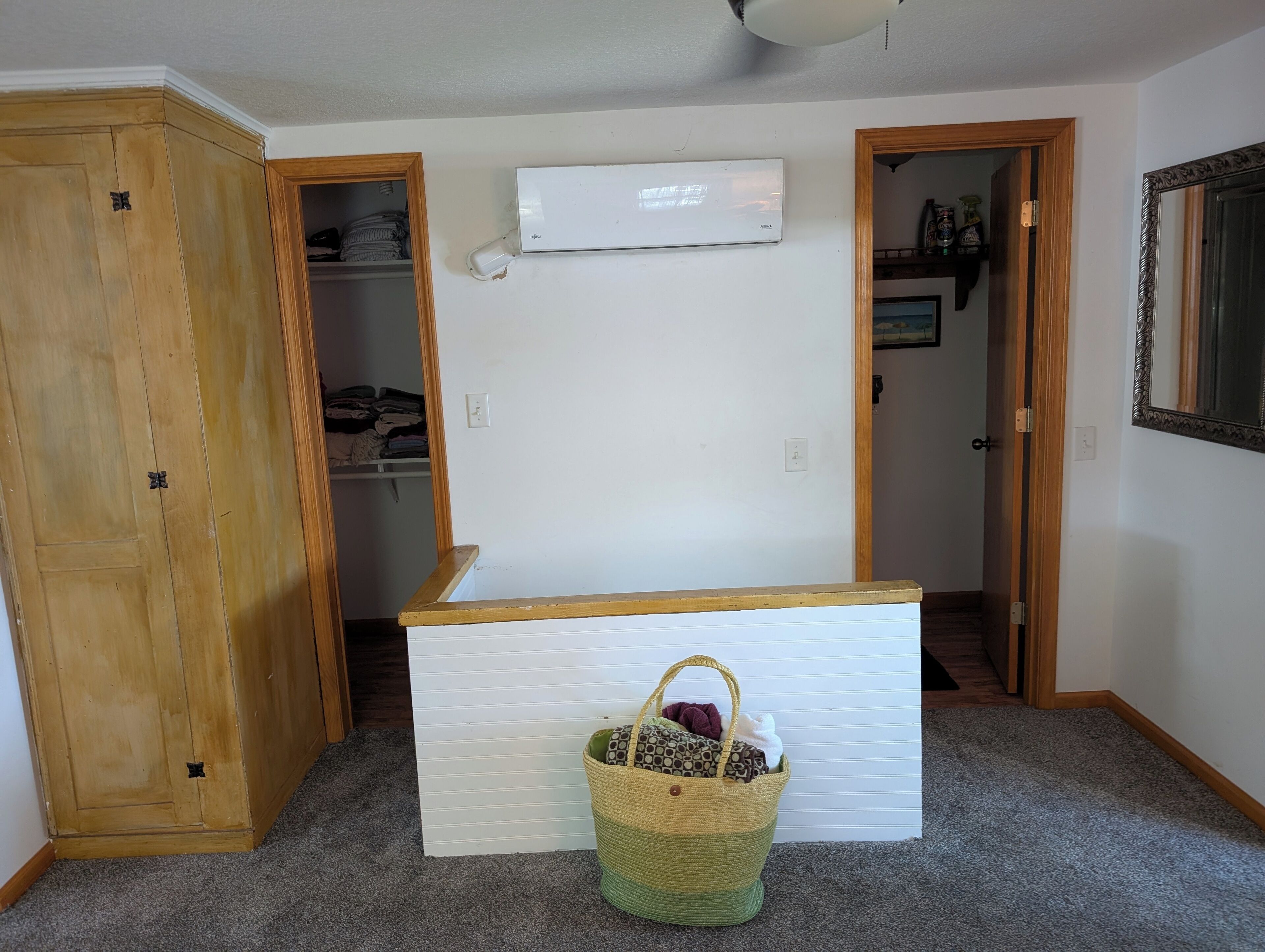 Quarto com guarda-roupa de madeira, penteadeira branca, cesto de vime e ar condicionado.