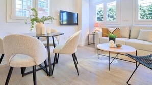 Una sala de estar moderna con comedor, un conjunto de sofás y un televisor montado en la pared.