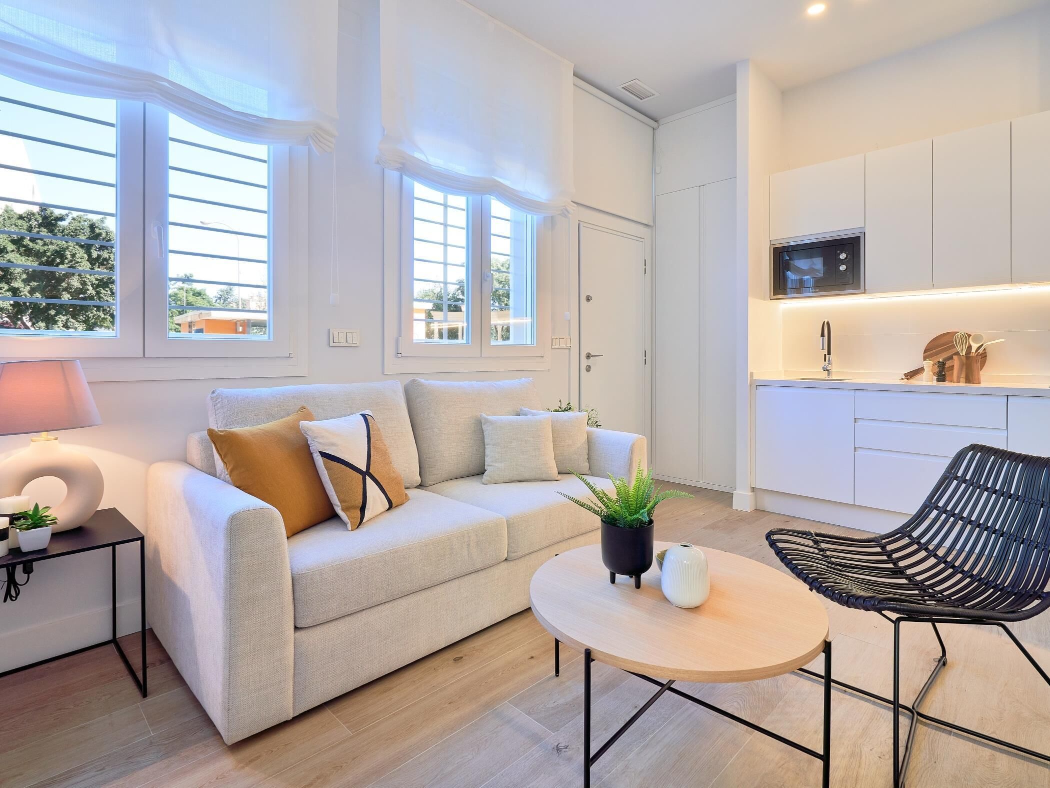 A modern living room with a sofa, a round coffee table, a black chair, and a small side table with a lamp and a plant.