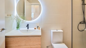 Un baño moderno con un espejo redondo, un lavabo, un inodoro y una zona de ducha.