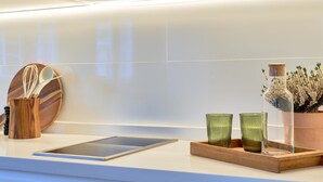 Una cocina moderna con encimera blanca, un utensilio de madera y una botella de vidrio con flores.