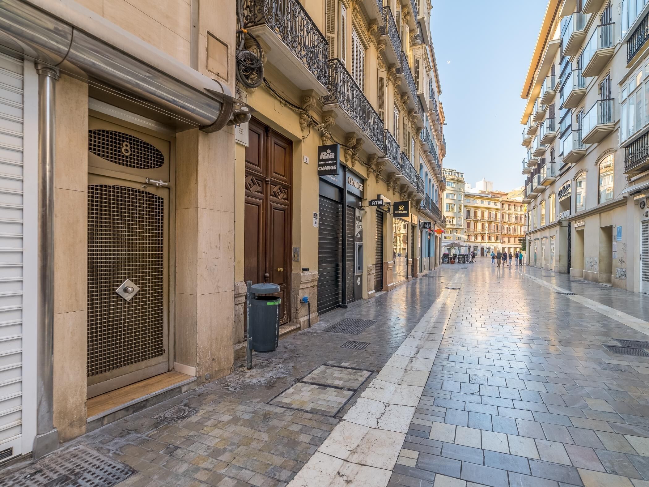 Une rue bordée d’immeubles, avec une poubelle et un magasin fermé.