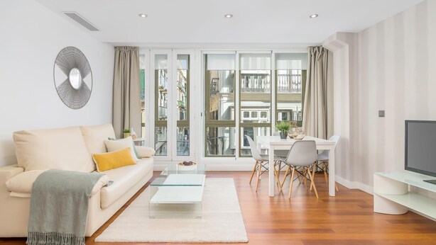 A modern living room with a sofa, coffee table, dining area, and a TV.