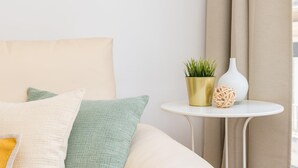A neatly arranged bedroom with a bed, pillows, a small round table with a plant and a vase, and a window with curtains.