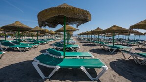 A beach with rows of green lounge chairs and thatched umbrellas. - iloftmalaga Playamar I (Torremolinos)