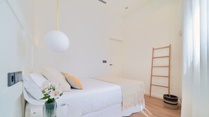 A minimalist bedroom with a white bed, bedside table with a vase of flowers, and a wooden ladder against the wall. - iloftmalaga Playamar I (Torremolinos)