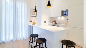 A modern kitchen with a white island, bar stools, pendant lighting, and a large window with sheer curtains. - iloftmalaga Playamar I (Torremolinos)