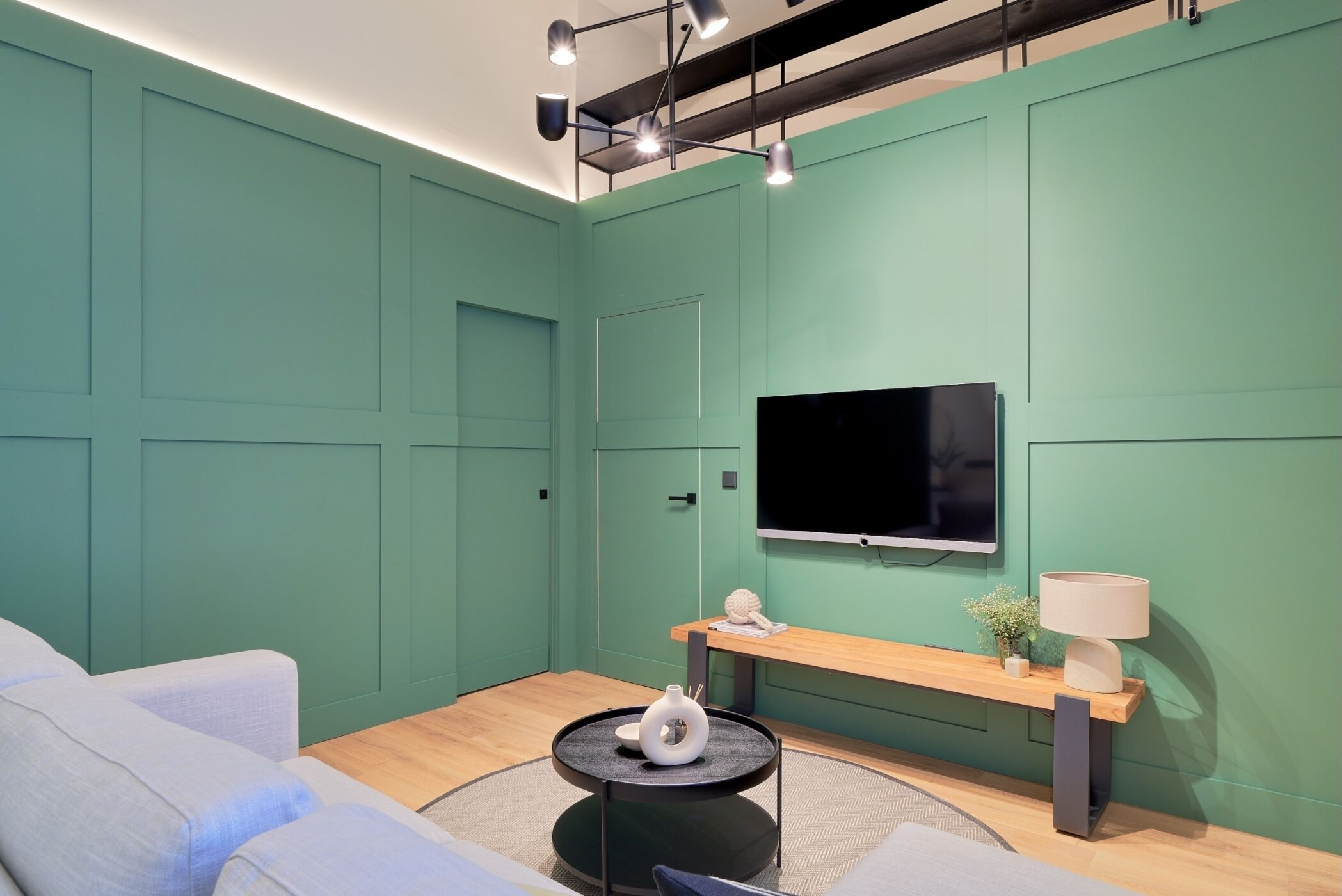 Un salon moderne avec des murs de couleur turquoise, un téléviseur à écran plat, une table basse ronde et des canapés de couleur claire.