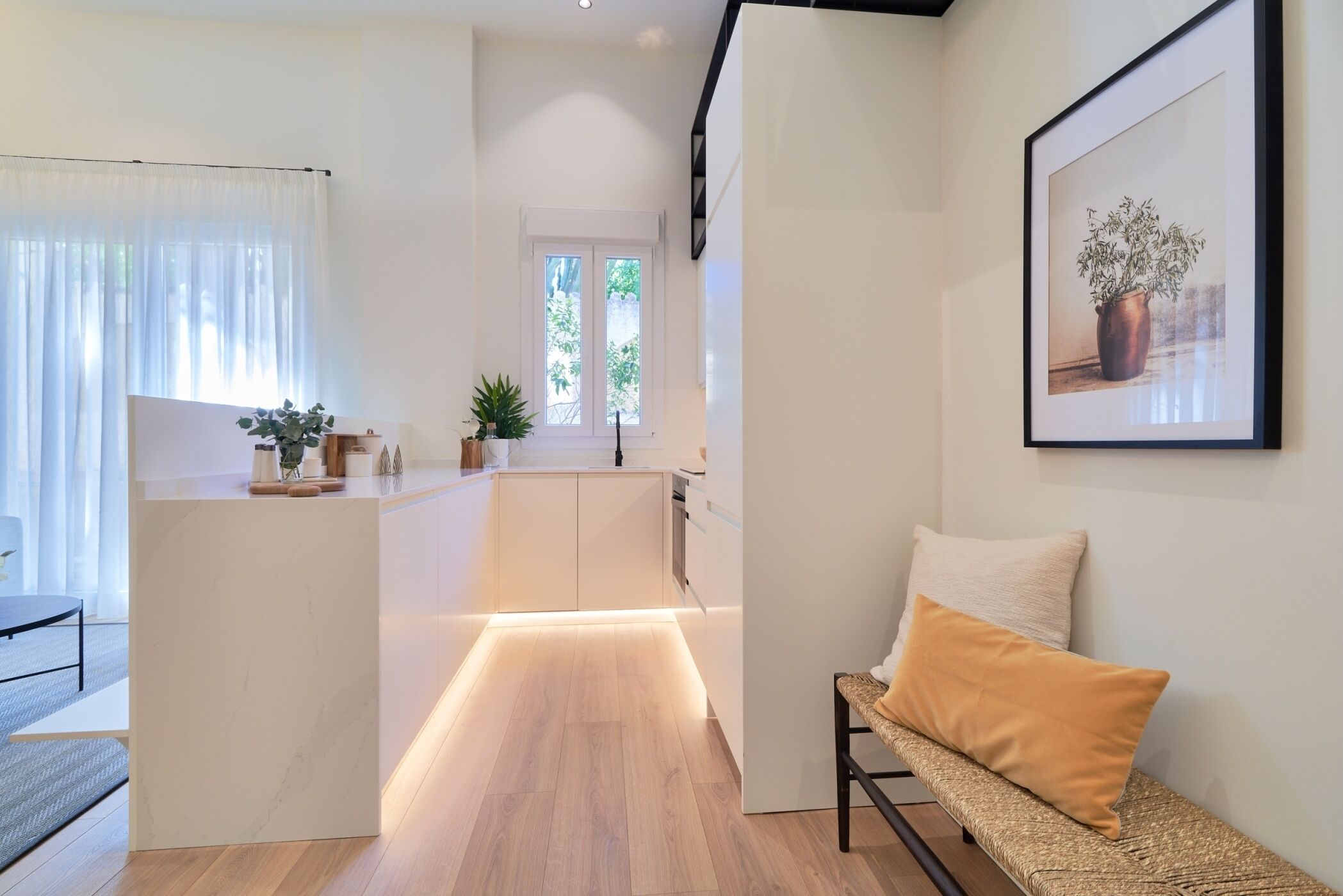 A modern kitchen with a central island, a dining area with a bench, and a framed artwork on the wall.