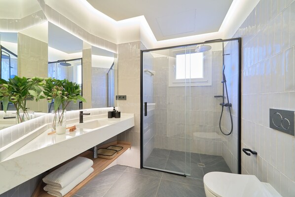 A modern bathroom with a glass-enclosed shower, a large mirror, and a vanity with a towel rack.