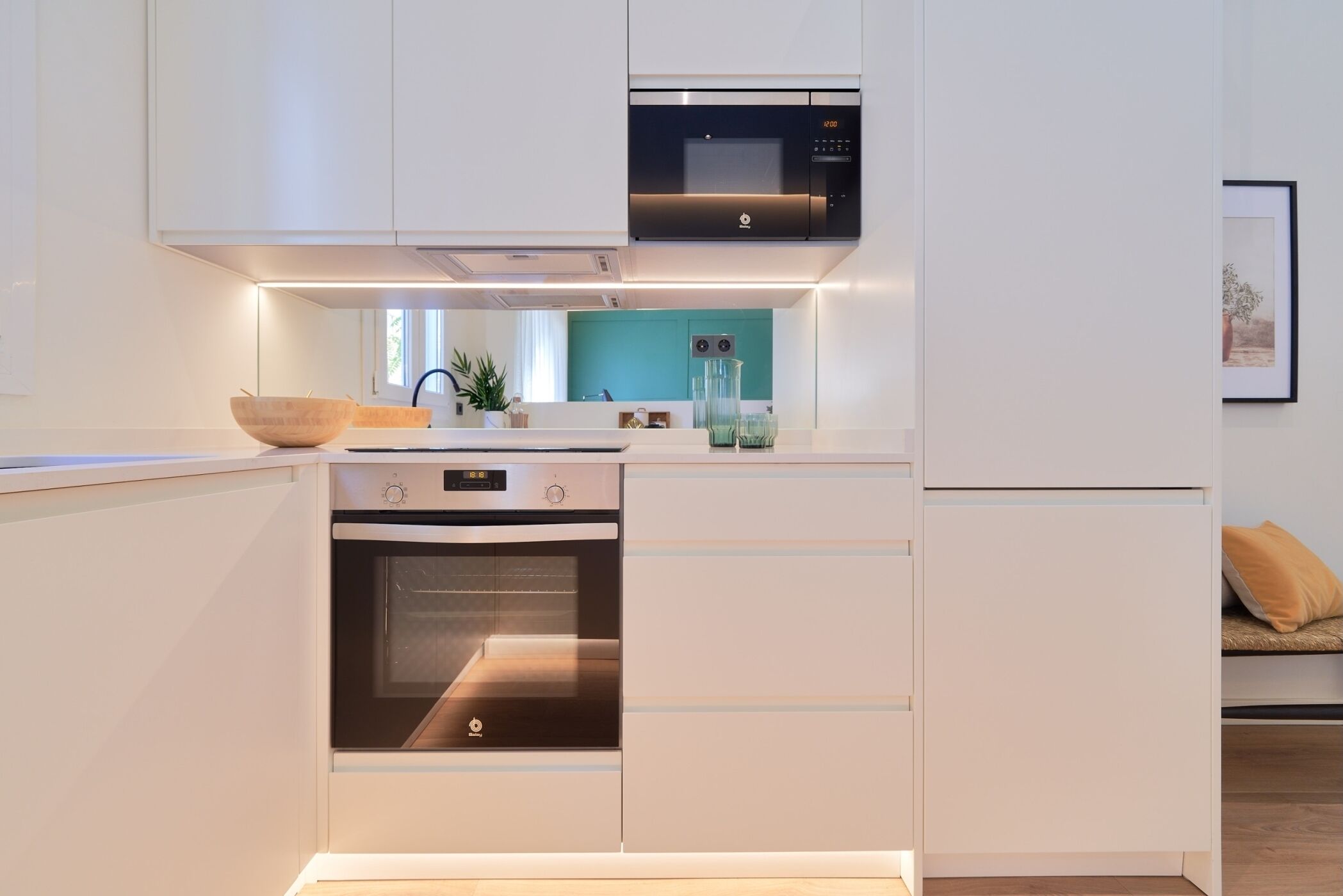 Une cuisine moderne avec des meubles blancs, un four encastré, un four à micro-ondes et un plan de travail sur lequel se trouvent un saladier et des récipients en verre.