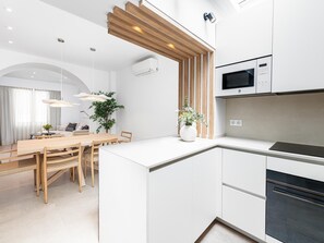 A modern kitchen with white cabinetry, a built-in microwave, and a black oven. There is a wooden dining table with chairs and a hanging light fixture above it.
