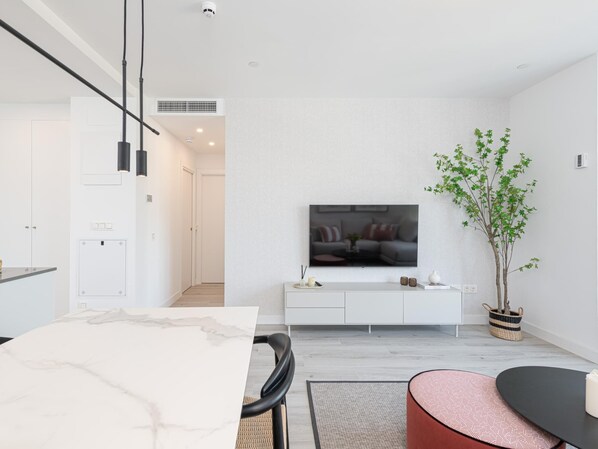 A modern living room with a flat-screen TV mounted on a white brick wall, a dining area with a marble table, and a potted plant.