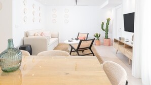 Een moderne woonkamer met een bank, een eettafel, stoelen, een televisie en decoratieve objecten.