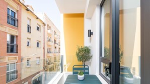 Een balkon met een tafel en stoelen, een bloempot en uitzicht op omliggende gebouwen.