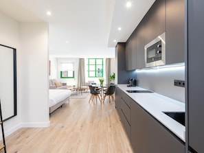 A modern hotel room with a kitchenette, a dining area, and a living space.