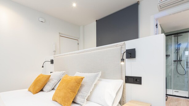 A modern bedroom with a large bed, bedside tables, a built-in shower, and a plain wall. - Barroso II - iloftmalaga (Málaga)
