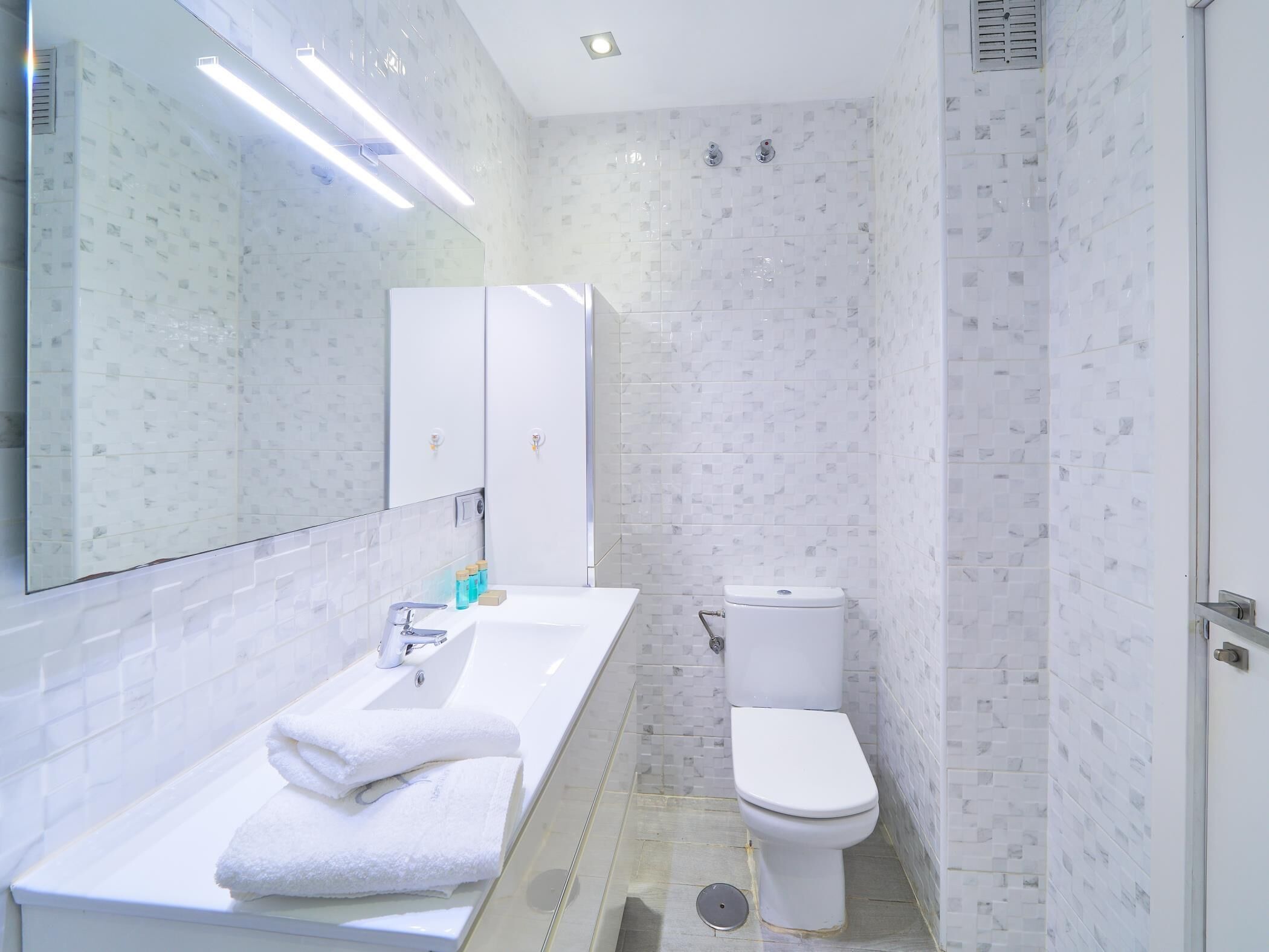 A modern bathroom with a white sink, mirror, and toilet.