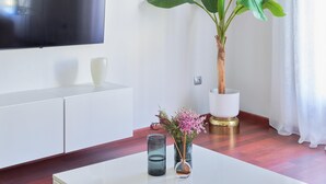 Una sala moderna con un televisor de pantalla plana montado en la pared, un armario blanco, una planta en maceta y una mesa de centro con objetos decorativos.