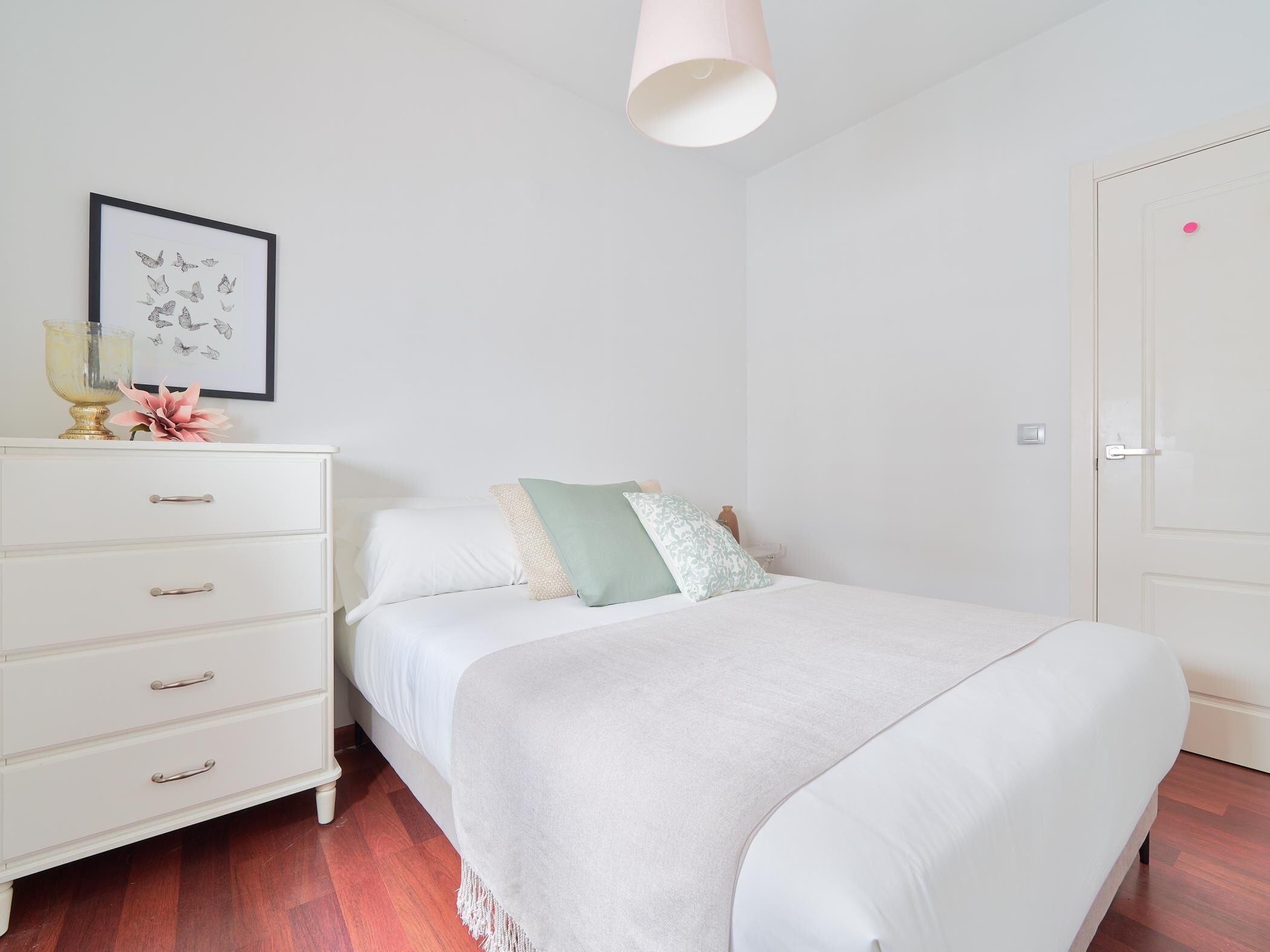 A neatly arranged bedroom with a bed, a dresser, a framed butterfly artwork, and a door.