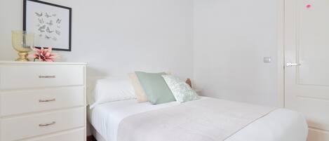 A neatly arranged bedroom with a bed, a dresser, a framed butterfly artwork, and a door.