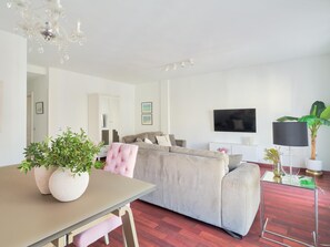 A modern living room with a beige sofa, a glass coffee table, and a dining table with two potted plants.