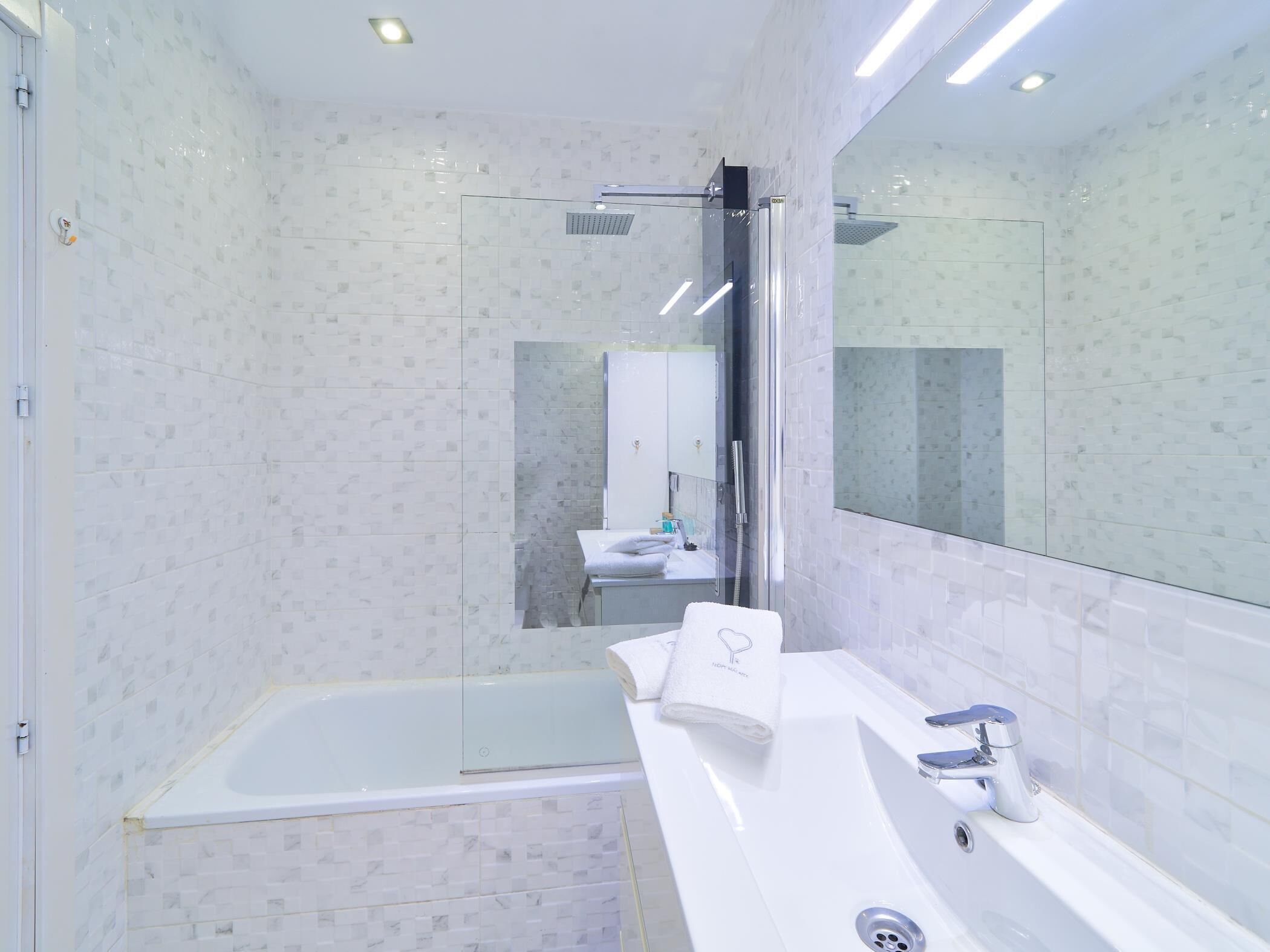 Une salle de bain moderne avec une douche à l’italienne en verre, une baignoire blanche et un grand miroir au-dessus du lavabo.