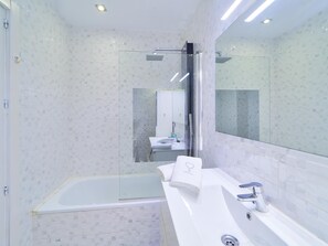 A modern bathroom with a glass shower enclosure, a white bathtub, and a large mirror above the sink.