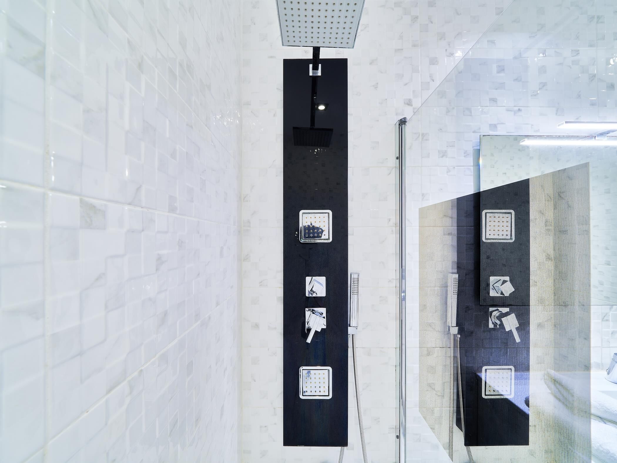 A modern bathroom with white marble tiles, a black towel rack, and a glass shower enclosure.