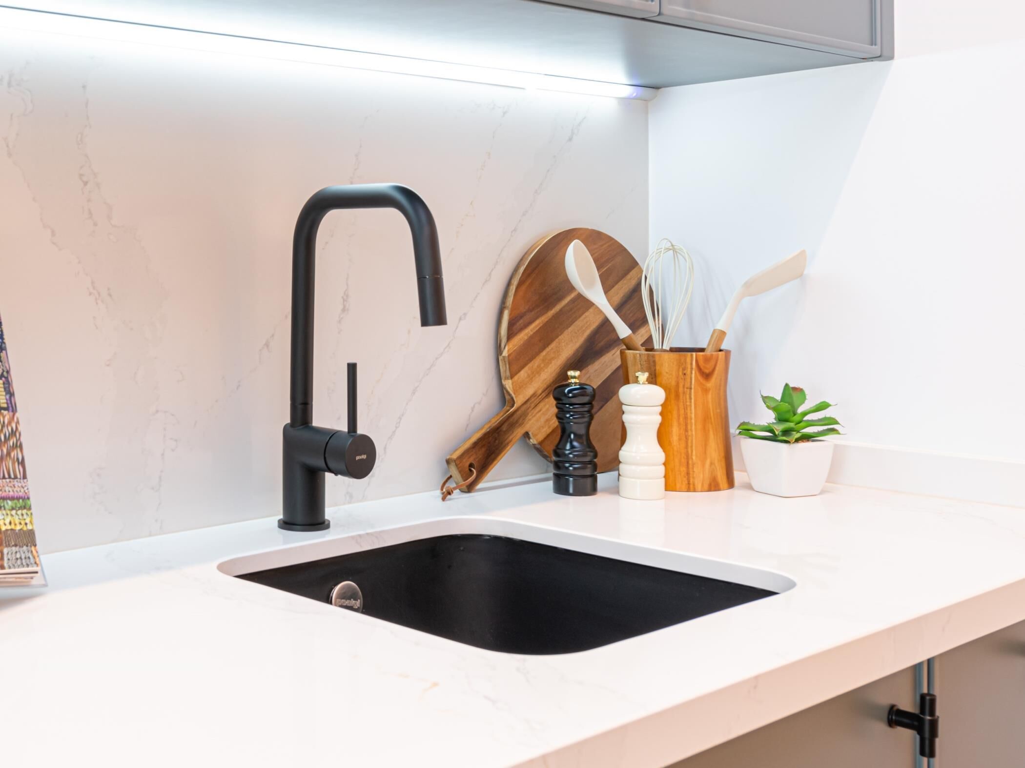 A modern kitchen with a black faucet, a wooden cutting board, a spice rack, and a small potted plant.