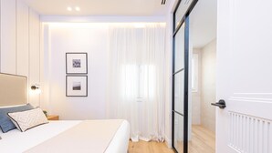 A modern bedroom with a large bed, a nightstand, a wall-mounted light, and two framed pictures.