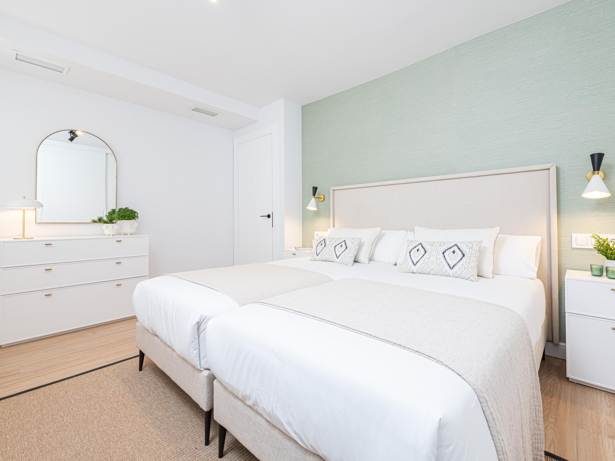 Un dormitorio moderno con dos camas, un tocador, un espejo y una mesita de noche con lámpara.