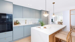 Una cocina moderna con armarios azul claro, una isla blanca y un horno empotrado. Hay luces colgantes sobre la isla y una silla de madera al final de la isla.