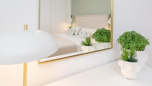 Un dormitorio moderno con un espejo grande, una mesita de noche, una cama con almohadas y dos plantas en macetas.
