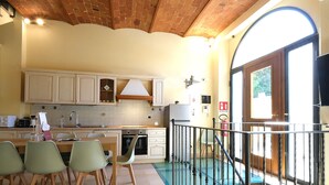 Eine Küche mit Holzausstattung, einem Esstisch mit Stühlen, einer Treppe mit Geländer und Blick ins Freie durch ein großes Fenster.
